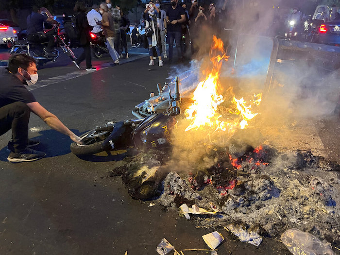 En esta imagen del lunes 19 de septiembre de 2022 tomada por una persona no empleada por "Associated Press" y obtenida por AP fuera de Irán, un hombre tira de una motocicleta policial incendiada durante una protesta por la muerte de una mujer que había sido detenida por incumplir el código de vestuario del país, en el centro de Teherán, Irán.