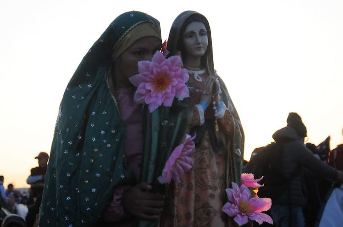 Una mujer caracterizada como la Virgen de Guadalupe sostiene una escultura durante el amanecer en la Basílica.