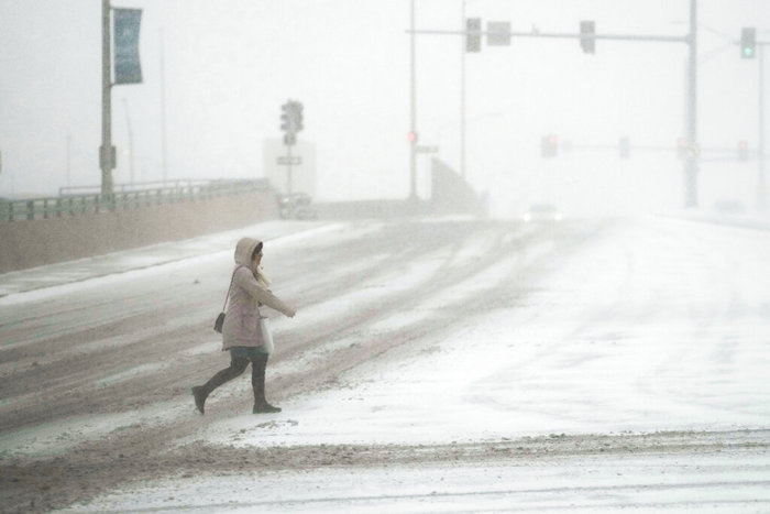 Una mujer cruza una calle en medio de una tormenta invernal, el jueves 22 de diciembre de 2022, en Rosemont, Illinois.