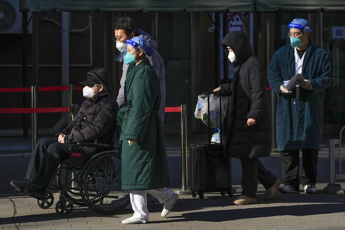 Personal médico con equipo de protección acompaña a un paciente anciano en silla de ruedas, seguido por familiares, a su salida de una unidad de fiebre en un hospital de Beijing, el lunes 19 de diciembre de 2022.