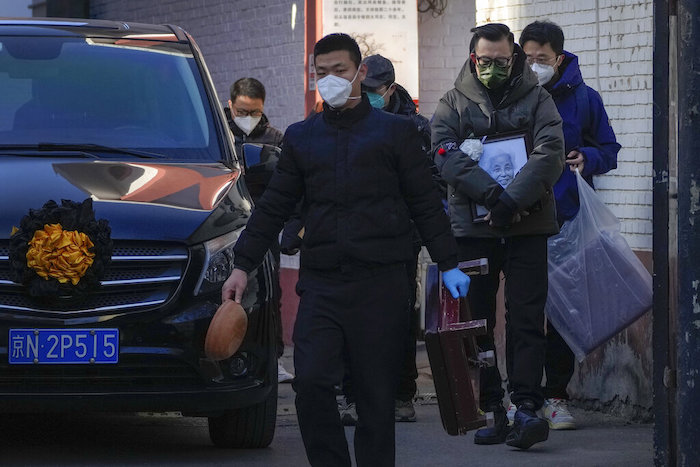Un familiar con la fotografía de una pariente fallecida camina junto a un vehículo que lleva el cuerpo ante una clínica para pacientes con fiebre en Beijing, el lunes 19 de diciembre de 2022.
