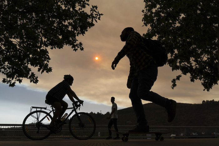 Varias personas, silueteadas contra un cielo cubierto por el humo de incendios forestales cercanos, caminan por un parque el viernes 16 de diciembre de 2022 en Santiago, Chile.