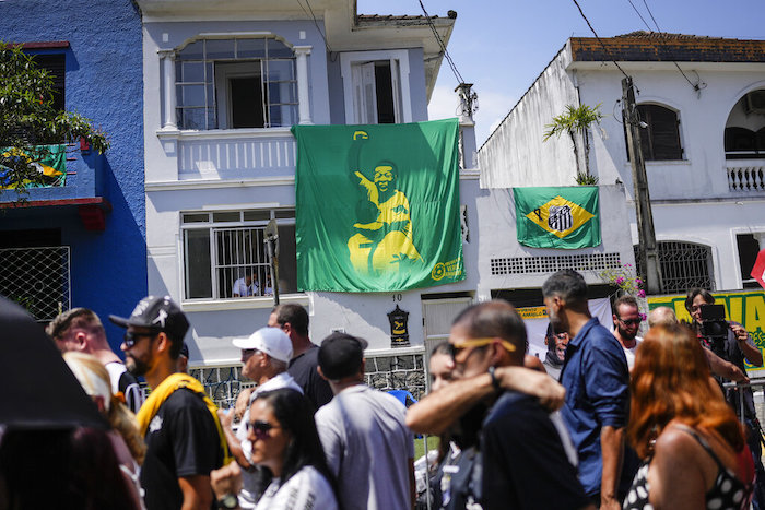 Una pancarta con la imagen de Pelé cuelga de una vivienda, detrás de la fila de gente que espera entrar al funeral en Santos, Brasil, el lunes 2 de enero de 2023.