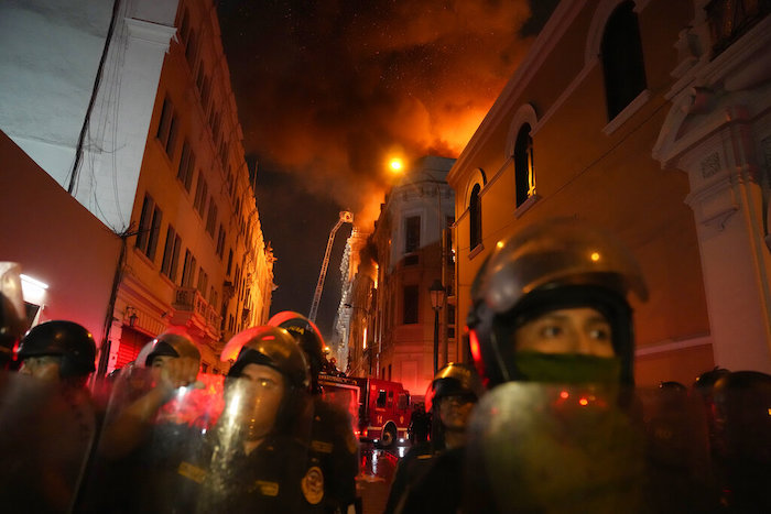 Policías antimotines bloquean una calle mientras un edificio arde a sus espaldas en una jornada de enfrentamientos contra manifestantes opositores en Lima, Perú, el jueves 19 de enero de 2023.