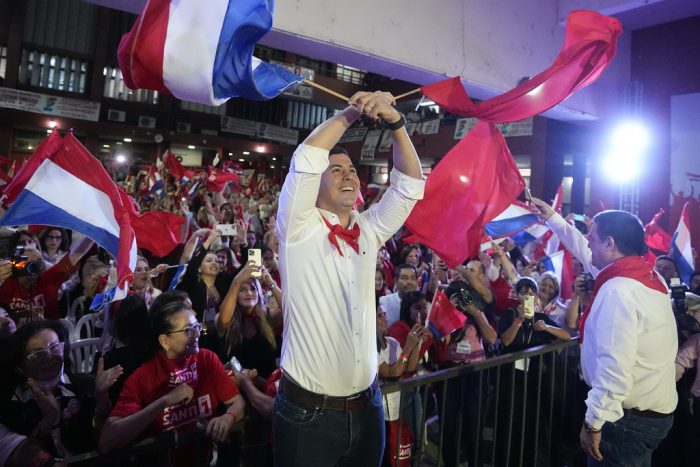 Santiago Peña, centro, candidato presidencial del partido Colorado, y el expresidente Horacio Cartes, derecha, sostienen las banderas de Paraguay y del partido en un mitin político en Asunción, Paraguay, el lunes 24 de abril de 2023.