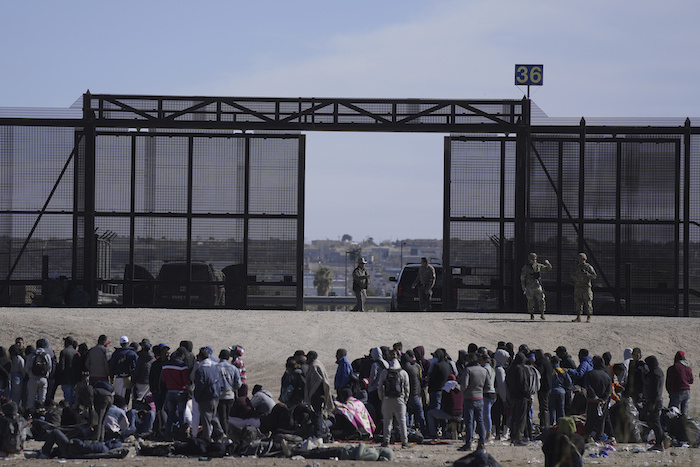Migrantes que cruzaron la frontera desde México hacia Estados Unidos esperan a un costado del muro fronterizo en donde agentes de la Patrulla Fronteriza de Estados Unidos montan guardia, el 30 de marzo de 2023, en una imagen tomada desde Cuidad Juárez, México.